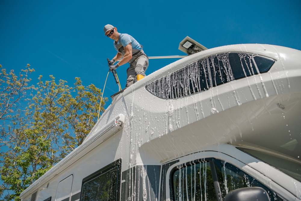 man standing on top of an rv cleaning the exterior of the vehicle