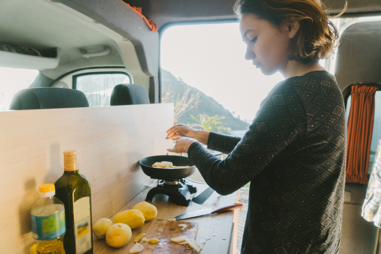 RV kitchen appliances - Young Caucasian woman cooking fried potato in the van