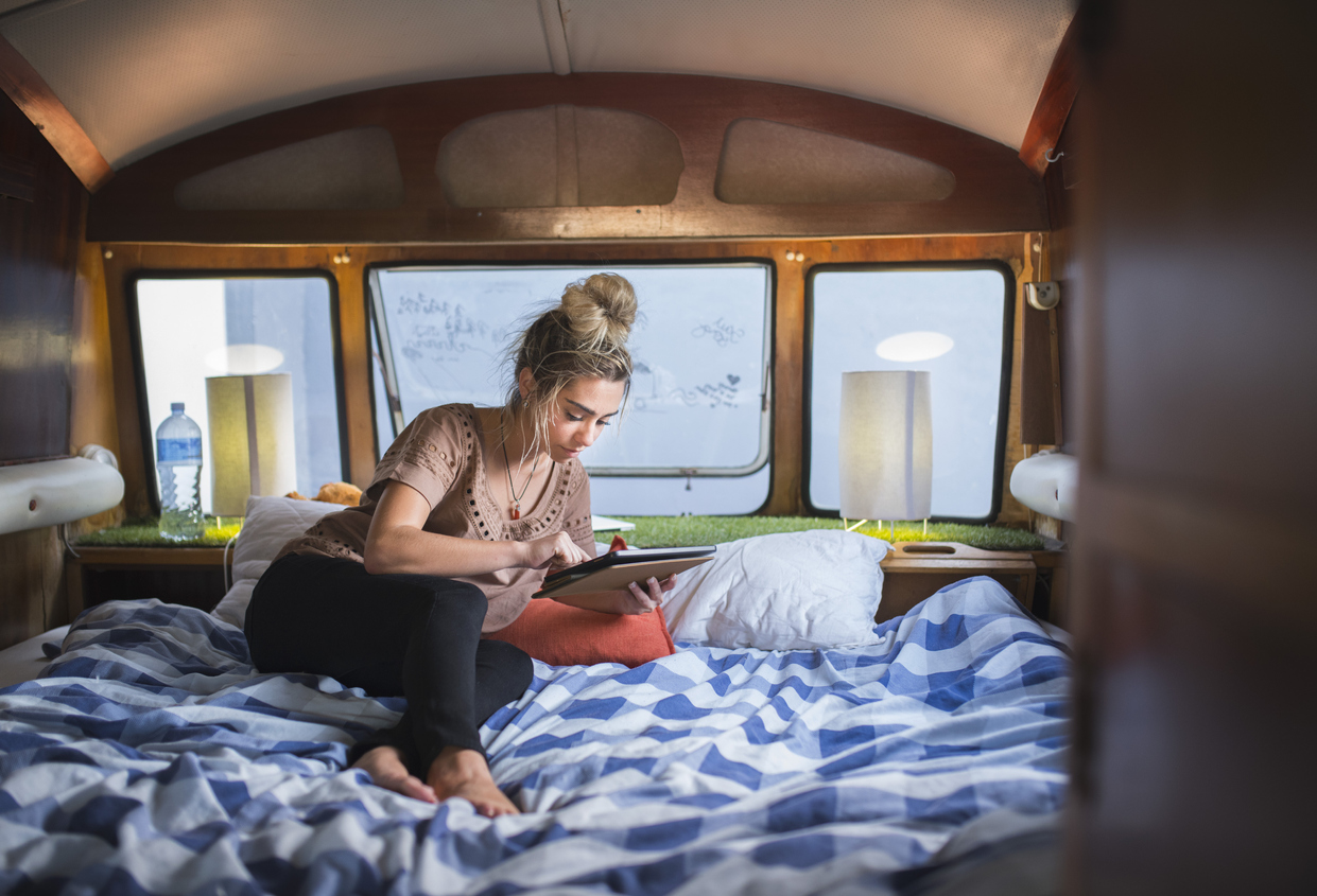 right RV furniture - Full length of young woman using digital tablet. Female hipster is leaning on bed in campervan. She is enjoying vacation.