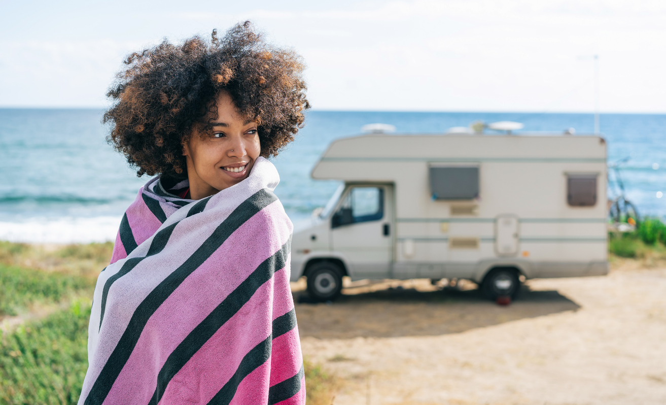 luxury RV resorts - Smiling afro women which is wrapped with a beach towel enjoying her summer vacation with camper
