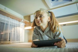 roadschooling - Caucasian Girl with Tablet Inside RV Camper Van. Road Travel with Multimedia.