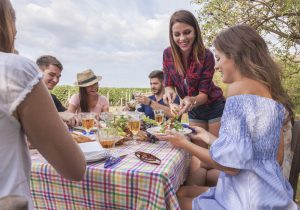 young adult friends have a picnic party outdoor beside a vineyard. they enjoy rose wine, seasonal simple food.