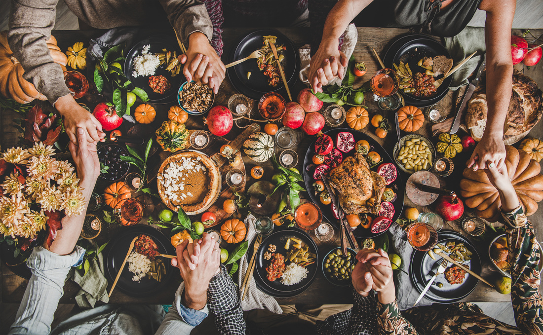 Family praying holding hands at an RV Thanksgiving table. Flat-lay of feasting peoples hands over Friendsgiving table with Autumn food, candles, roasted turkey and pumpkin pie over wooden table, top view