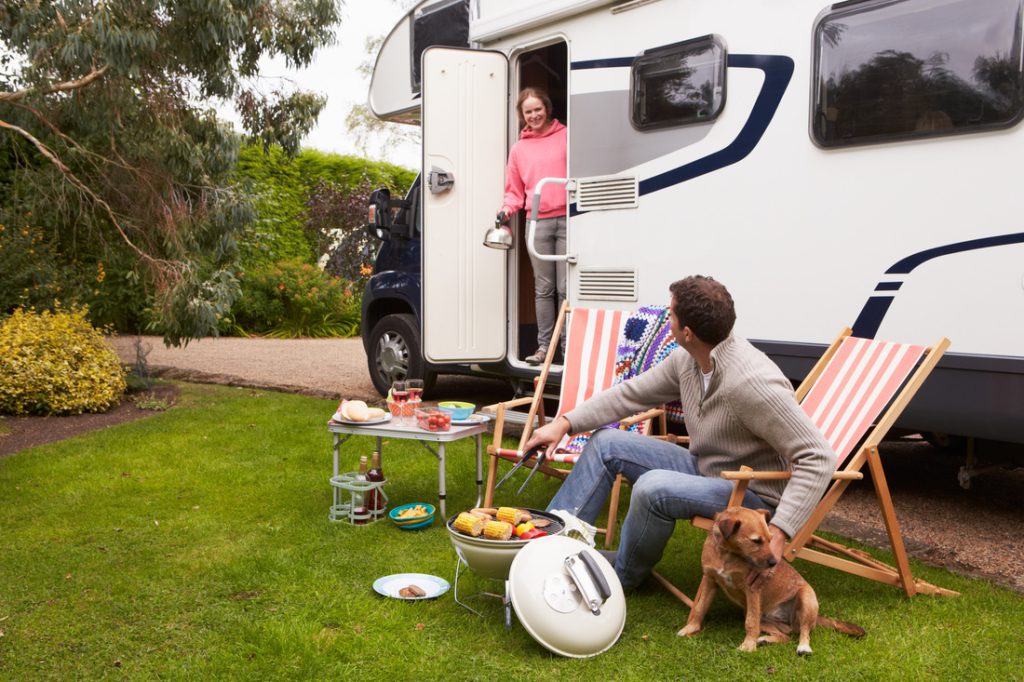 Couple eating outside their RV with a dog sitting nearby.