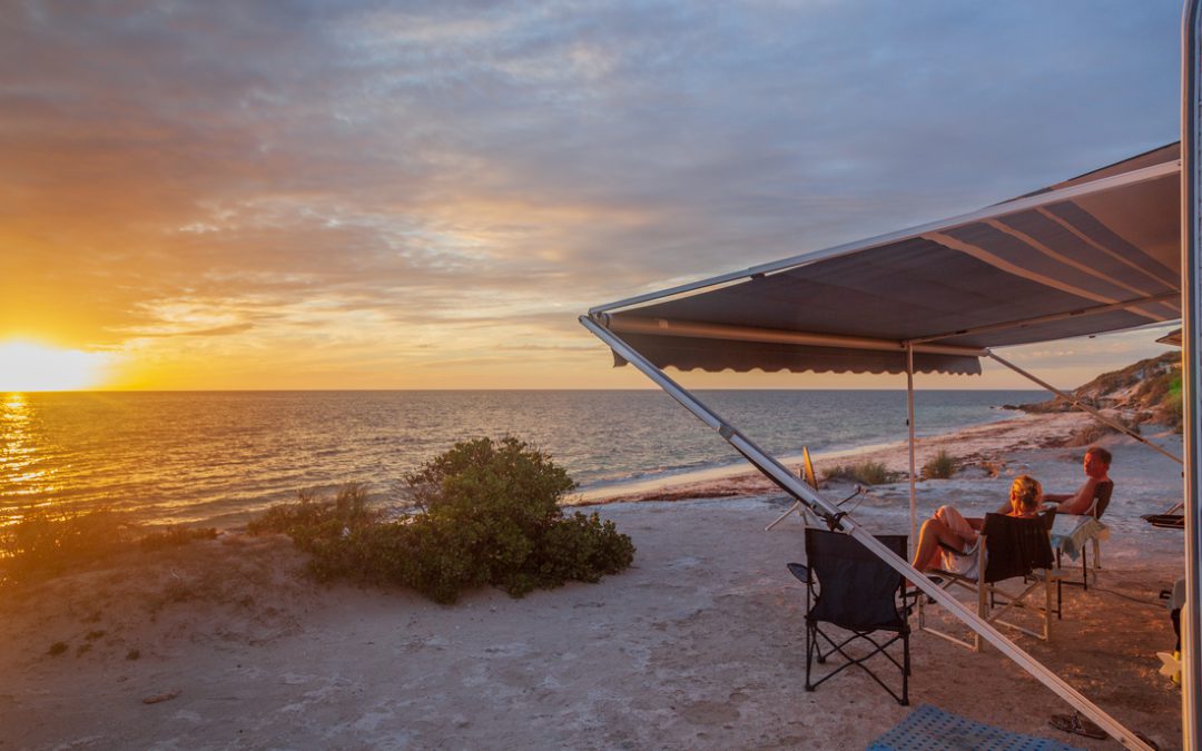 Retired couple sitting under the RV awning enjoying a wine next the beach with a golden sunset.