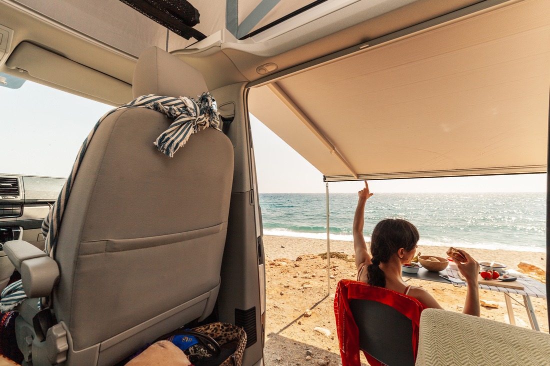 A young woman having breakfast in her caravan observing a good view of the beach