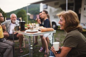 A family with a full-time RV budget sitting outside of their motorhome enjoying a meal. 