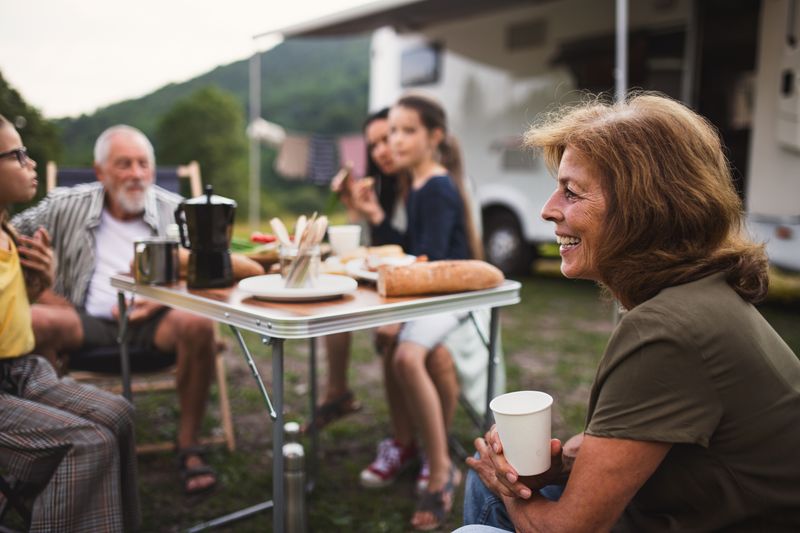 A family with a full-time RV budget sitting outside of their motorhome enjoying a meal.