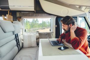 A man sits at the RV dinette booth on his laptop performing RV remote jobs. 