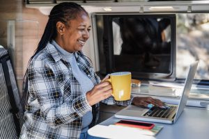 A senior woman performs one of our best RV remote jobs -- teaches from an RV. She holds a coffee mug and sits in front of a laptop. 