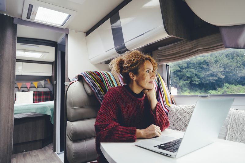 A woman performing remote RV jobs on her laptop at the booth dinette. Woman is looking out the window.