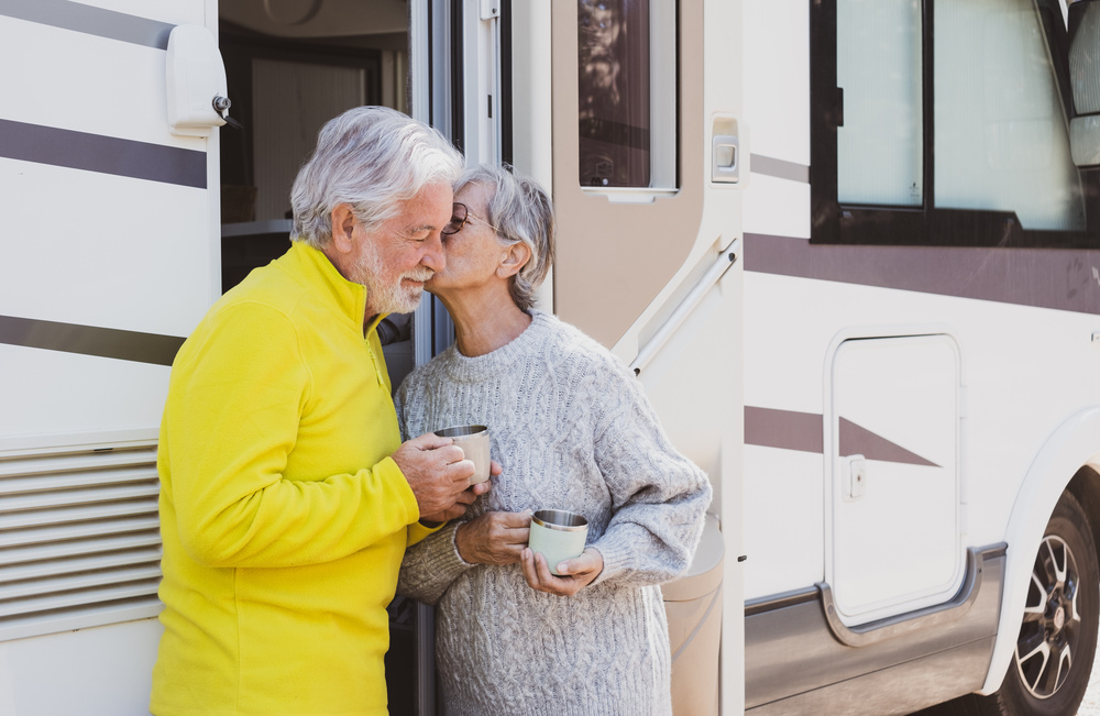 A senior couple stands happily outside of their Class A motorhome.