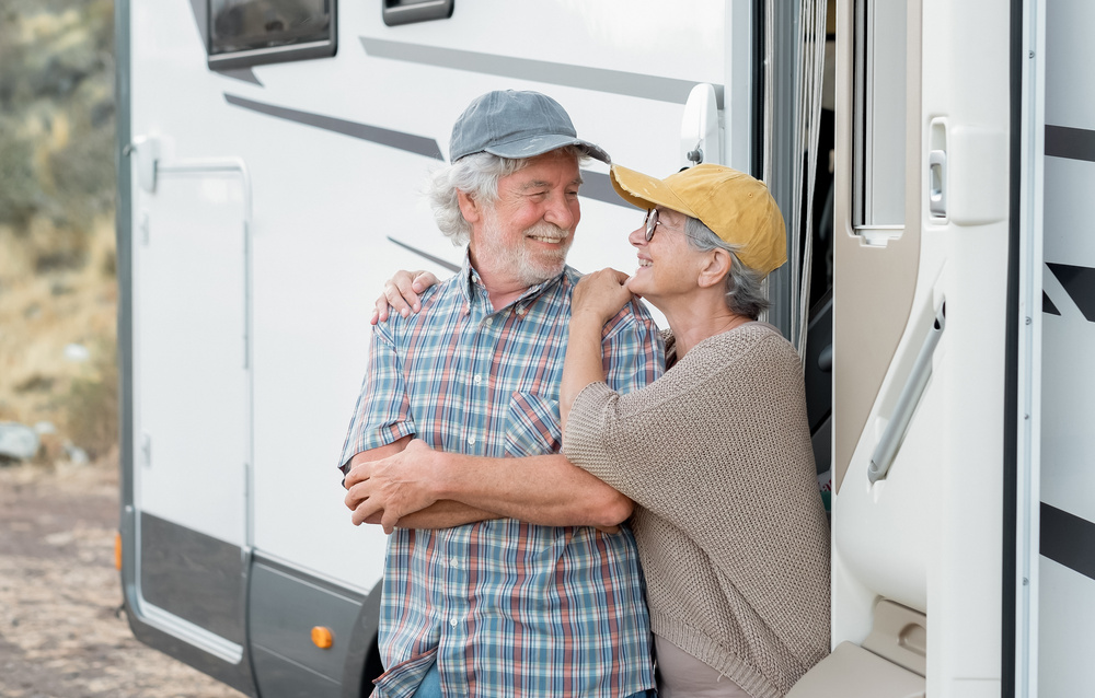 An older couple stand happily outside of the door of their Class A Motorhome.