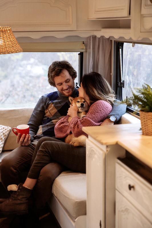 A couple sits inside of their RV as they cuddle a dog. 