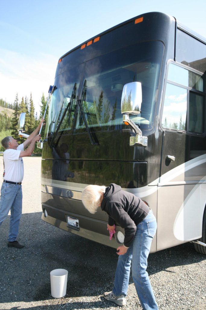 A couple wipes down the front of their Class A motorhome.