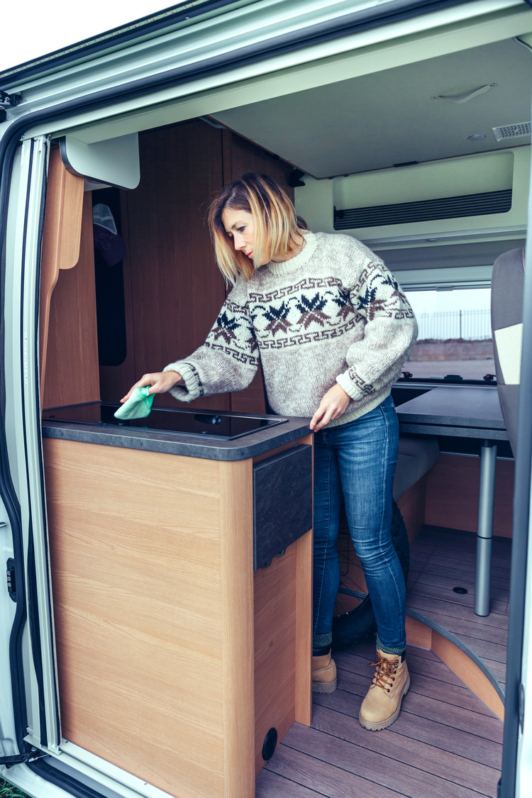 Young woman cleaning kitchen of a camper van with a cloth